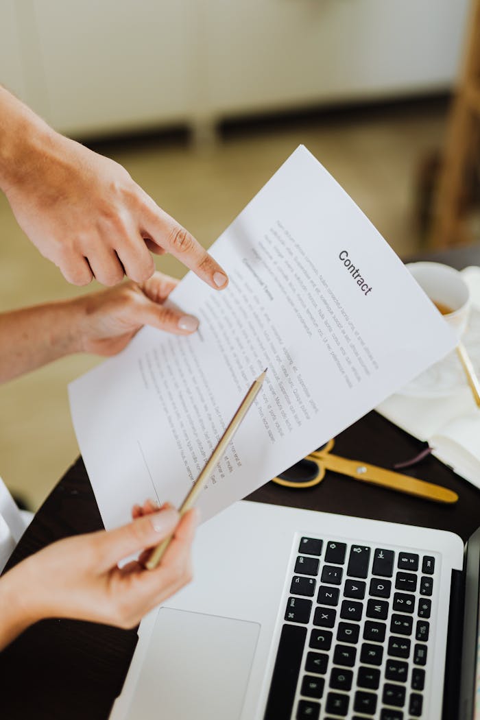 Hands pointing at contract on desk with laptop, indicating collaboration