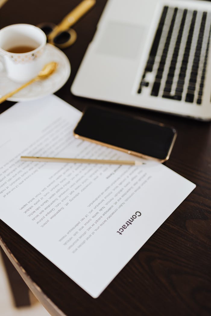 Close-up of a contract, smartphone, laptop, and coffee on an office desk.